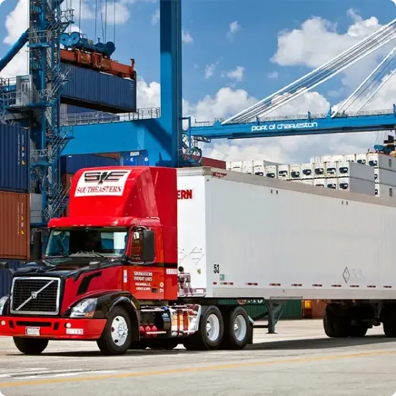 Red semi-truck at Port of Charleston with shipping containers and crane loading cargo in background