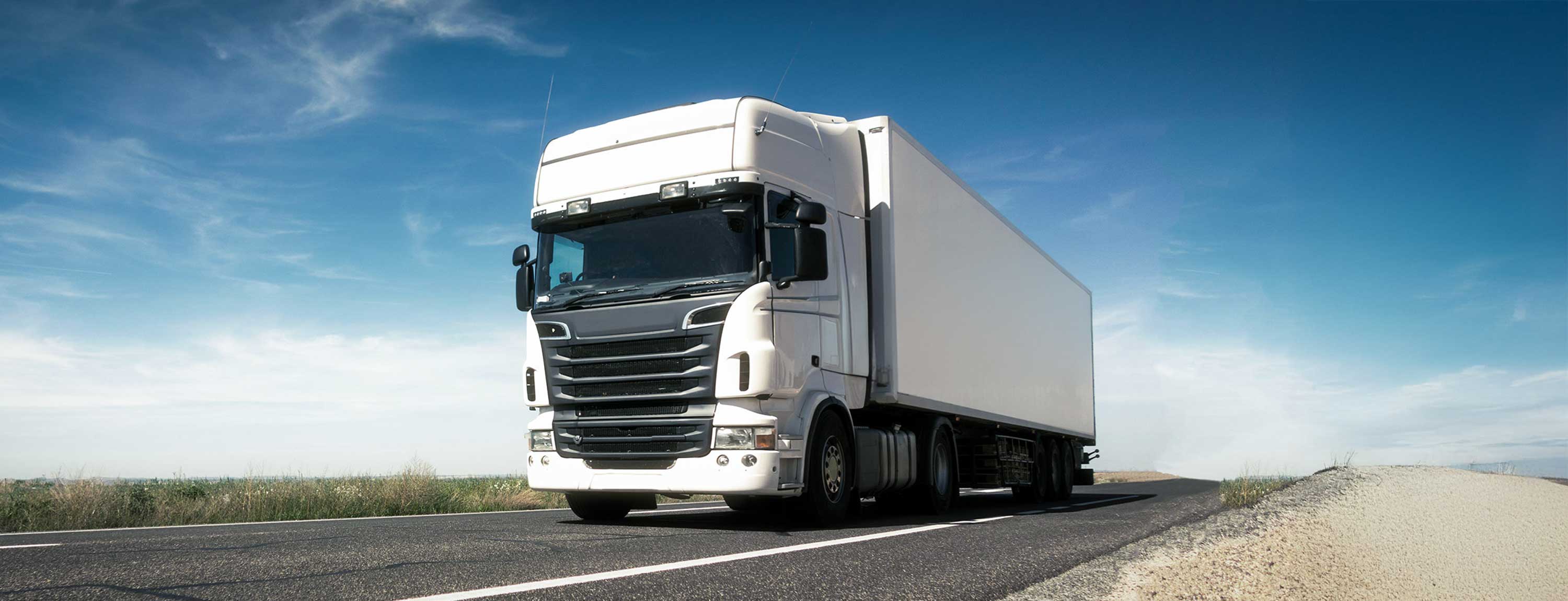 Aerial view of truck parking with numerous semi-trucks with white trailers parked in organised rows with yellow lines.