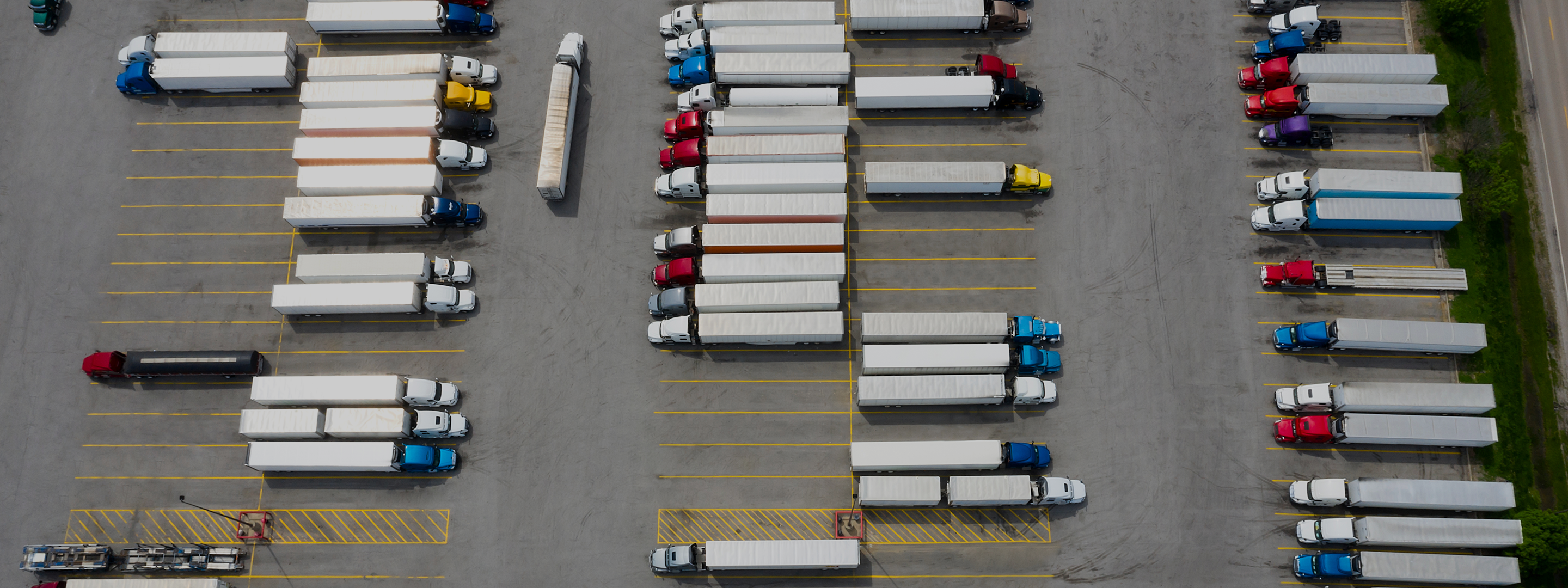Vista de estacionamiento de camiones con semirremolques y remolques blancos en filas organizadas con líneas amarillas.