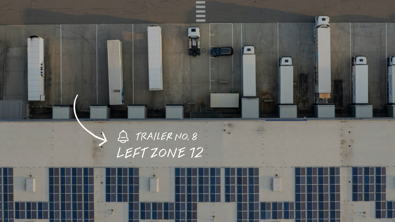 Aerial view of a warehouse loading dock with white trailers, labelled Trailer No. 8, Left Zone 12, with solar panels below.
