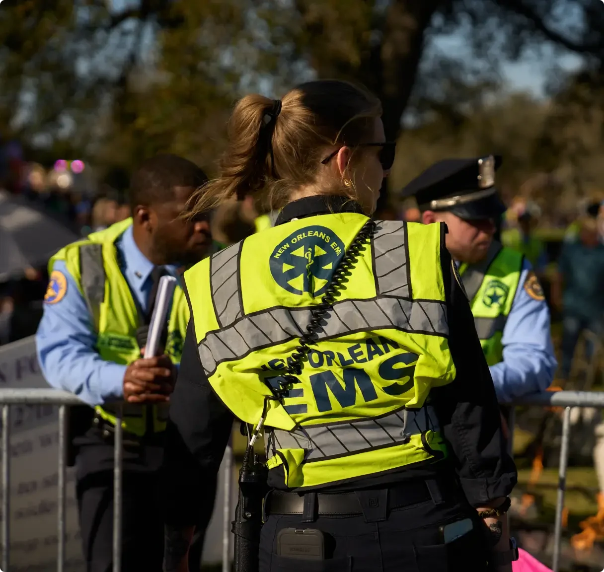 New Orleans EMS personnel in bright yellow safety vests working at an outdoor public event with police officers nearby.