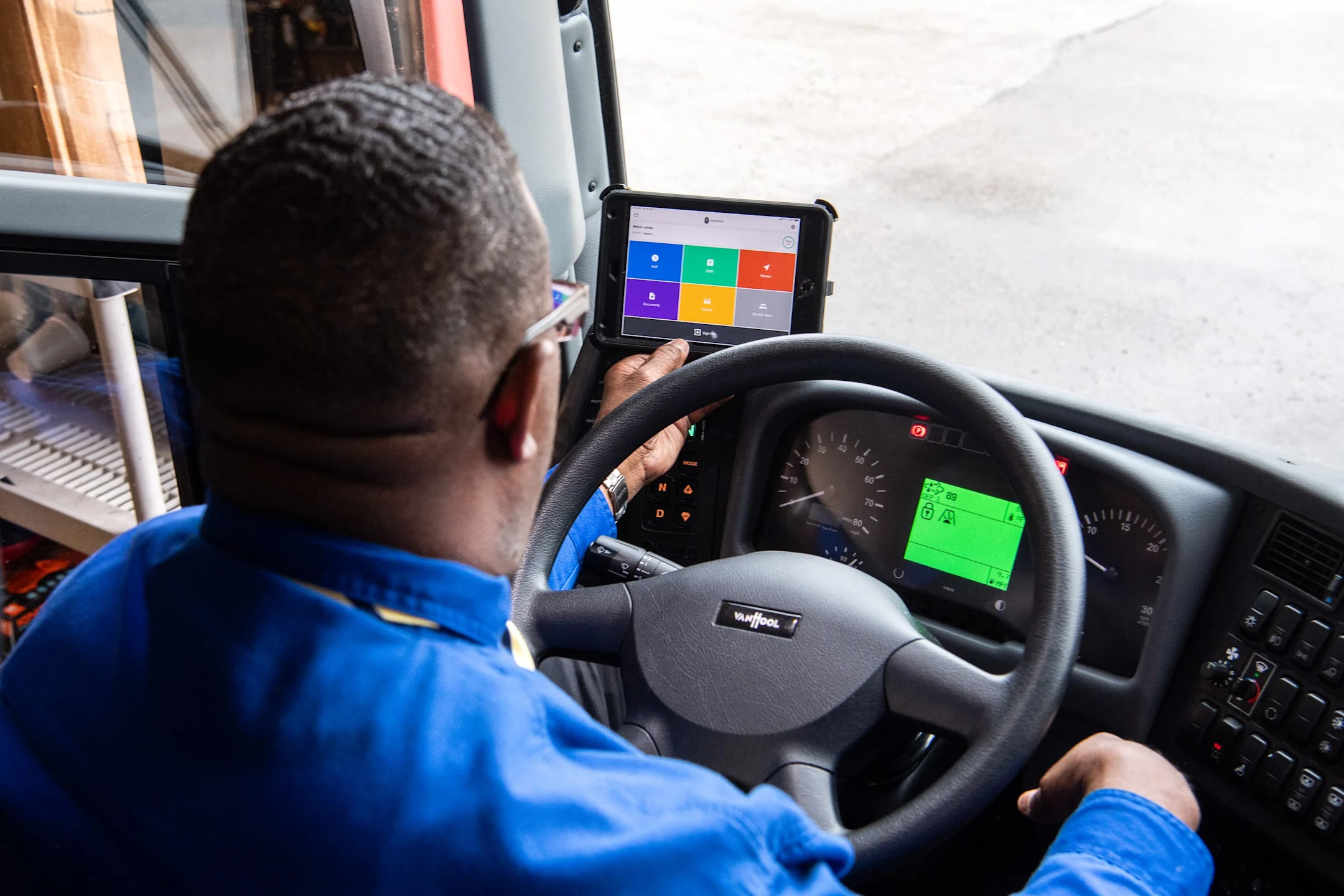 Buschauffeur in blauw uniform bedient een tablet met kleurrijke interface naast het stuurwiel in een moderne bus.