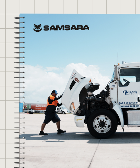 Monteur in oranje vest inspecteert motor van witte vrachtwagen. Samsara-logo zichtbaar op notitieboekje.