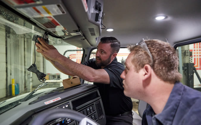 Two people inside the cab of a truck installing a dash cam.