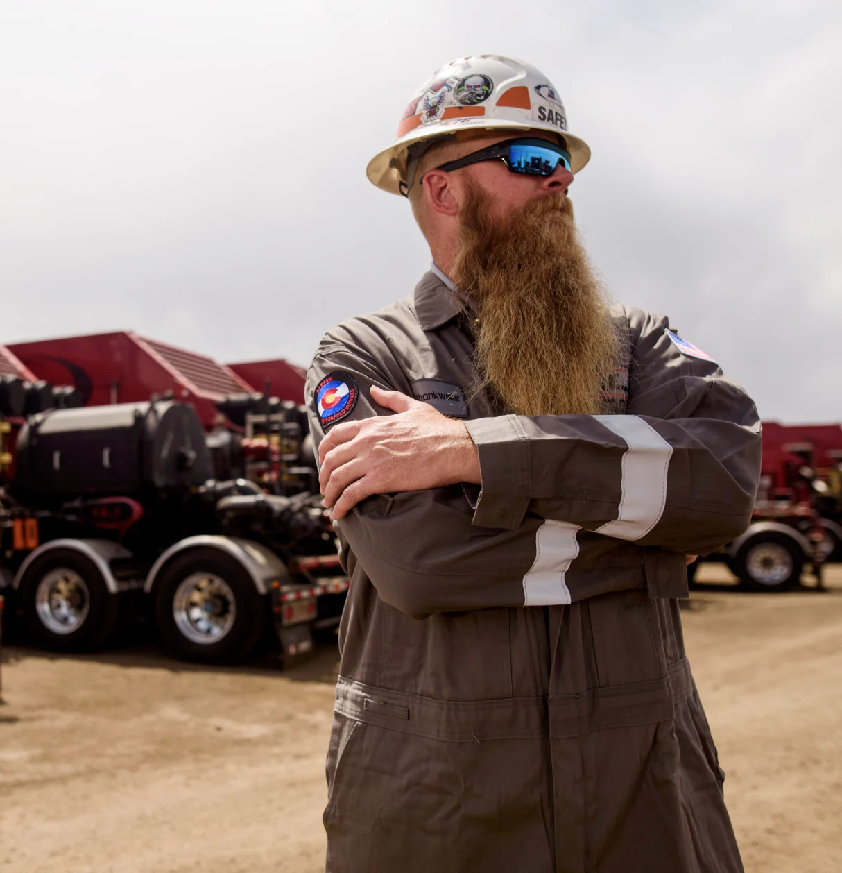 A Liberty Energy employee standing with crossed arms and looking off into the distance with a row of oil tankers behind him.
