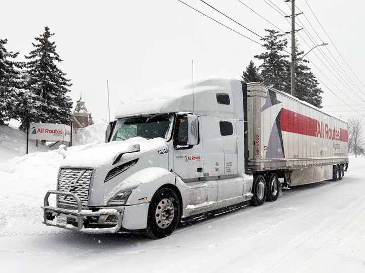 While All Routes Logistics truck on snowy street in front of yard