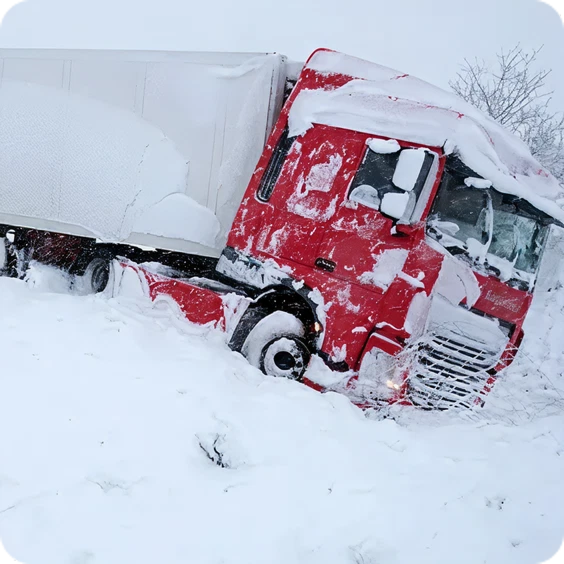 Red semi-truck stuck in deep snow on a winter road, with snow covering the cab and surrounding area.