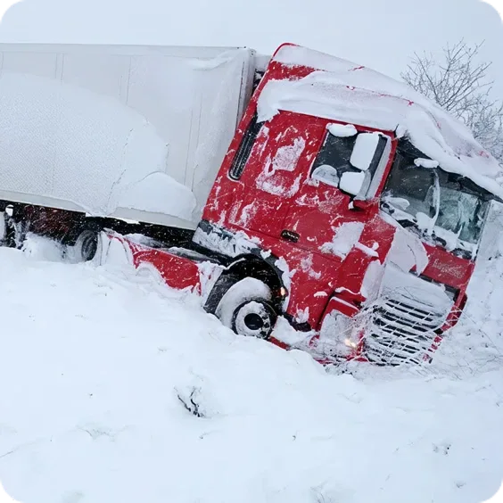 Red semi-truck stuck in deep snow on a winter road, with snow covering the cab and surrounding area.