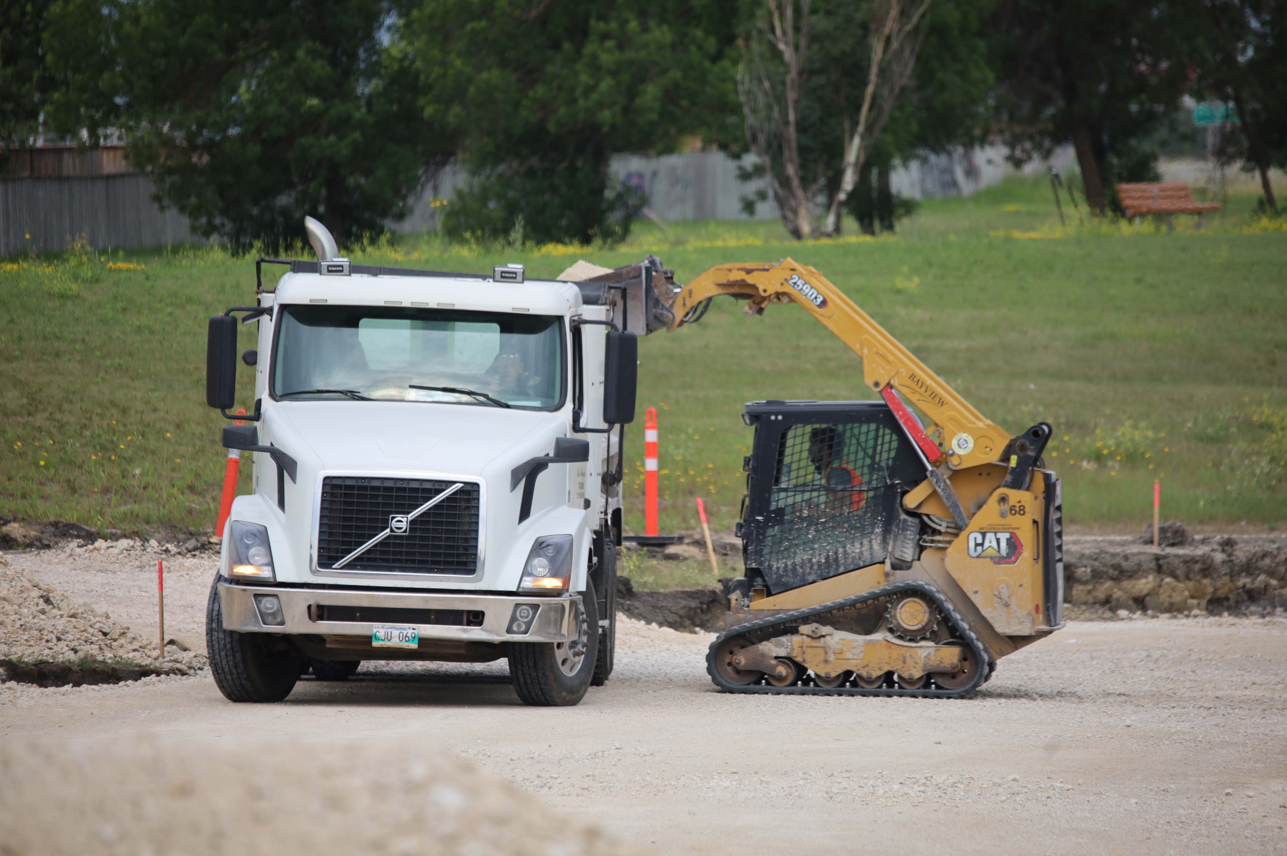 Un camion-benne Volvo blanc à côté d’un chargeur compact CAT jaune sur un site de construction avec des cônes de sécurité.