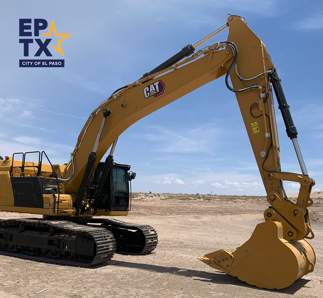 Excavadora amarilla CAT en desierto con logo de la ciudad de El Paso en la esquina superior izquierda contra un cielo azul.
