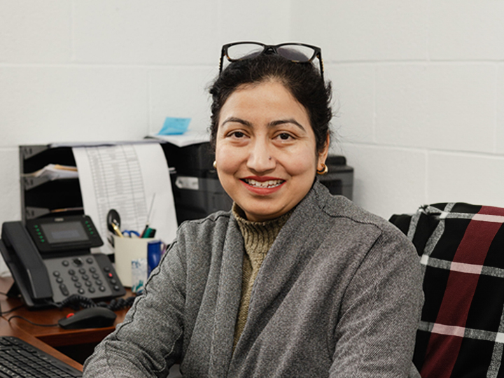 Woman with glasses sits at office desk smiling with scarf on chair