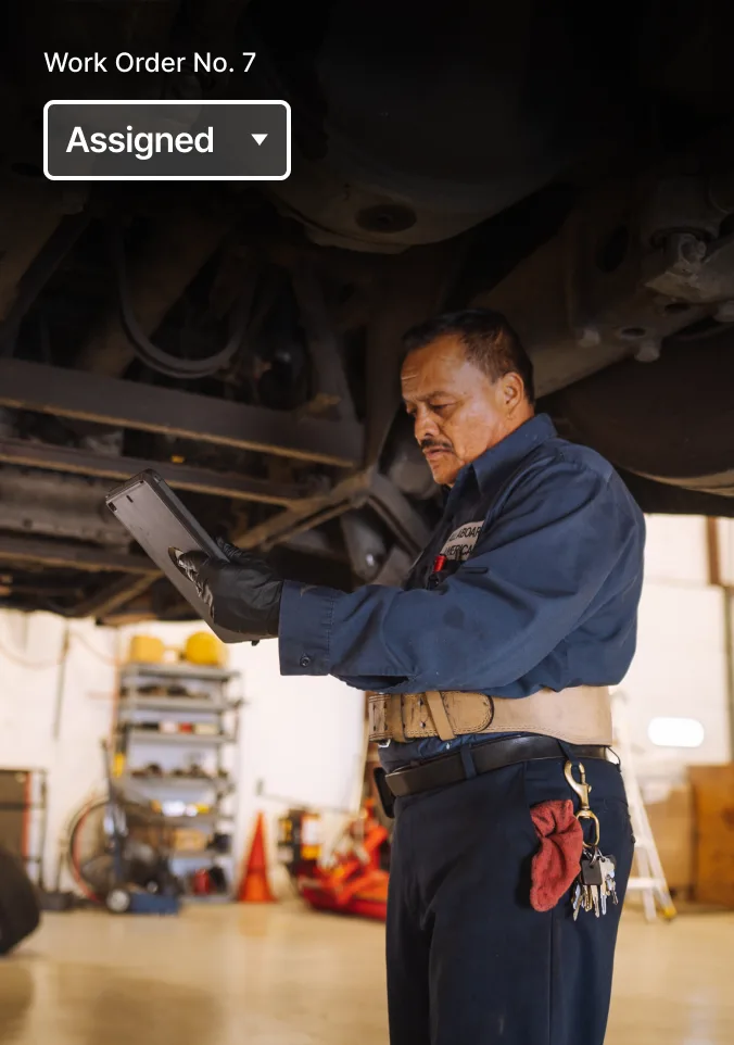 Two mechanics review work order status on a mobile phone.