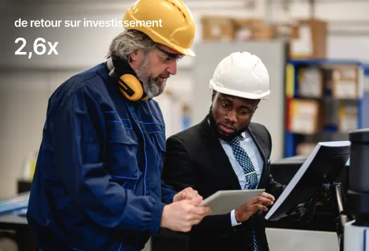 Deux ouvriers avec casques examinent des documents dans un environnement industriel. Texte : « ROI 2,6x » apparaît à gauche.