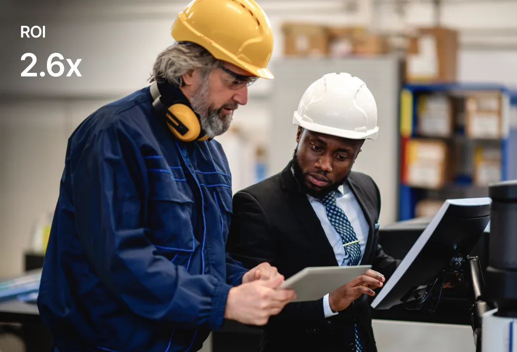 Zwei Arbeiter mit Schutzhelmen überprüfen Dokumente in einer industriellen Umgebung. Text: „ROI 2,6x“ erscheint links.