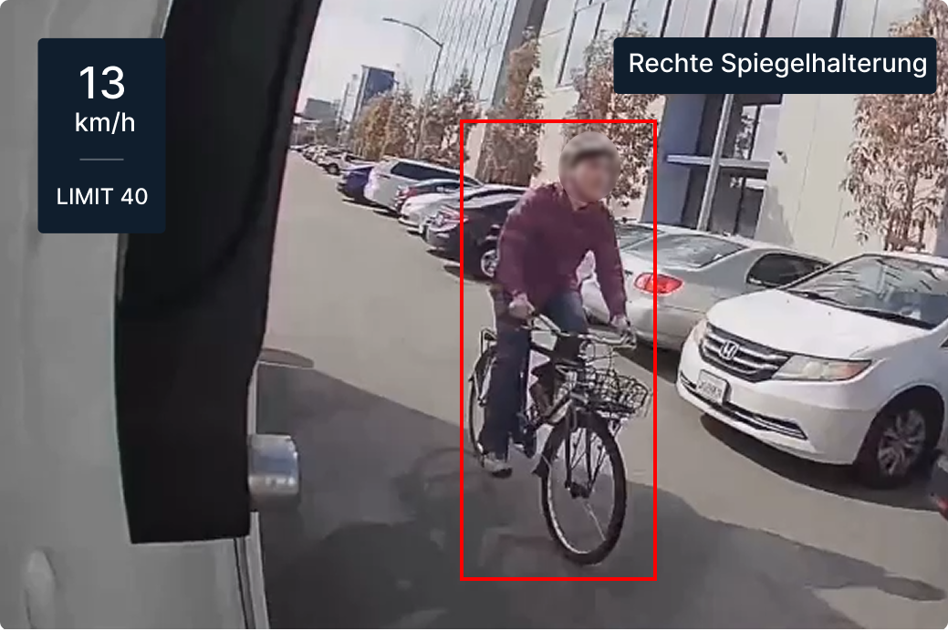 Dashboard-Straßenansicht mit Radfahrer und geparkten Autos; Geschwindigkeitsanzeige zeigt 13 km/h in einer 25-km/h-Zone.