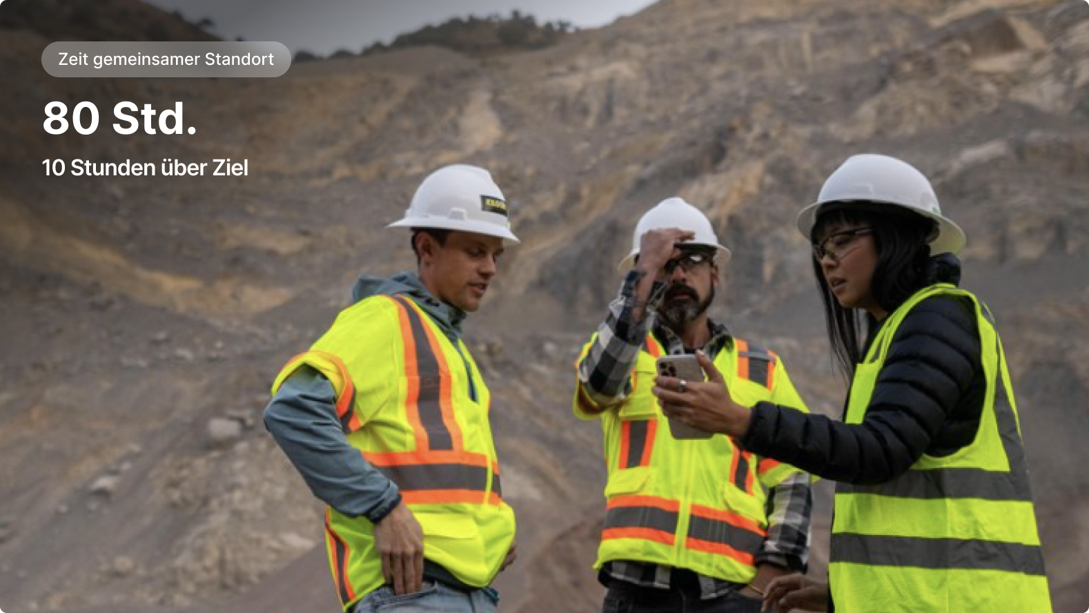 Drei Arbeiter in Schutzhelmen und Sicherheitswesten diskutieren an einem Steinbruch. Co-Standort-Zeit „80 h“ wird angezeigt.