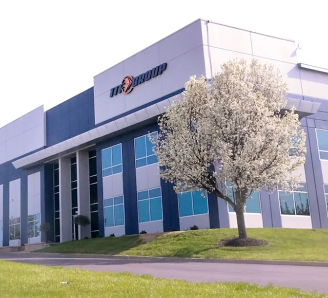 Modern office building with blue and white exterior, company logo on facade, and flowering tree in the foreground.