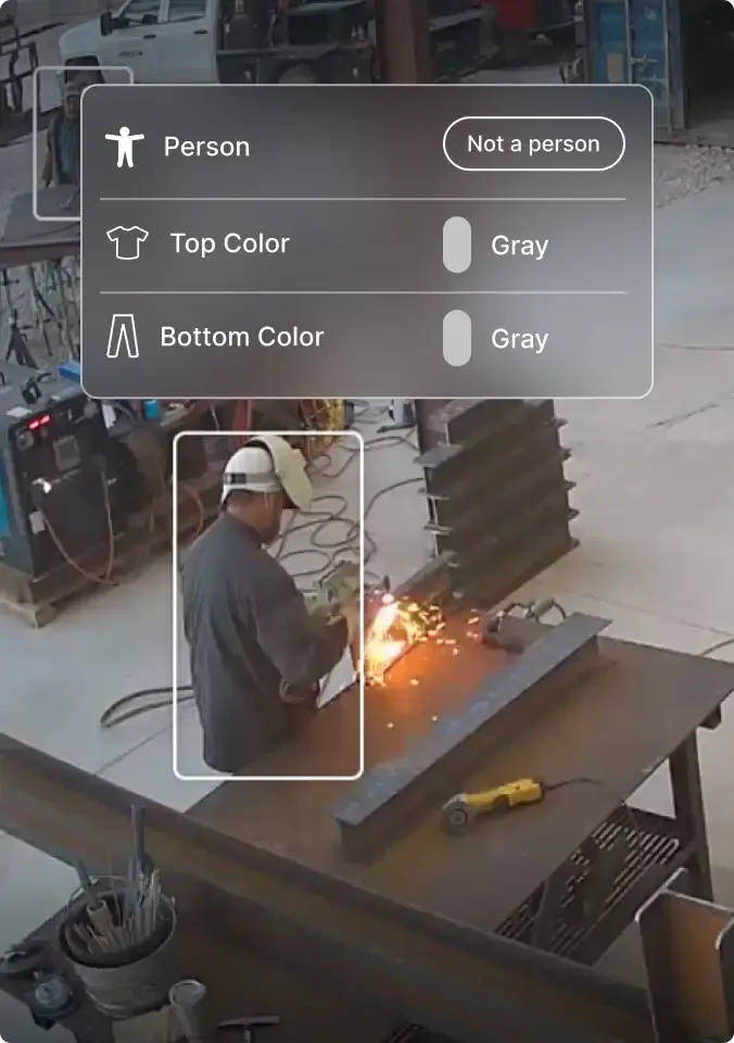 Security camera view of workshop with sparks from welding or cutting on workbench, person detection overlay visible.