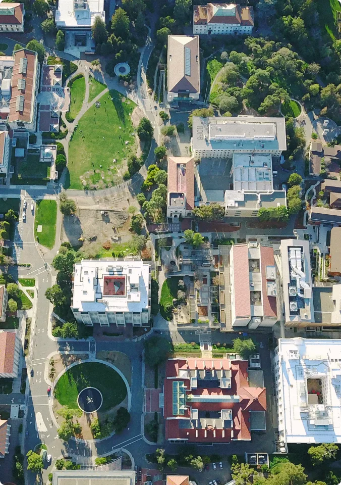 Aerial view of a university campus with buildings, green spaces, pathways, and circular plazas surrounded by trees.