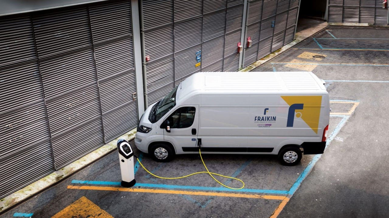 Quatre fourgons de livraison blancs portant la marque Fraikin garés sur un parking entouré d'arbres verts sous un ciel bleu.