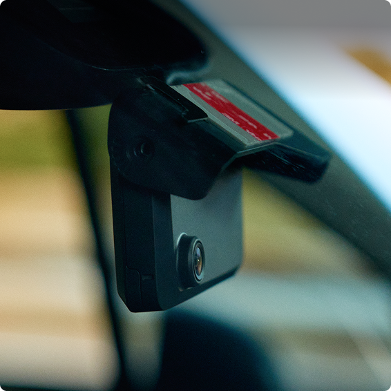 Dashboard camera mounted on car windshield with small red label, showing lens pointed toward road.