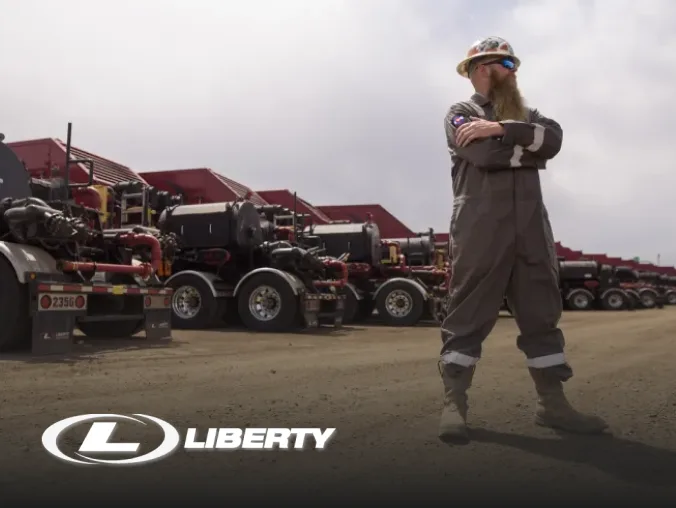 Liberty Energy worker standing proudly in front of row of fleet trucks.
