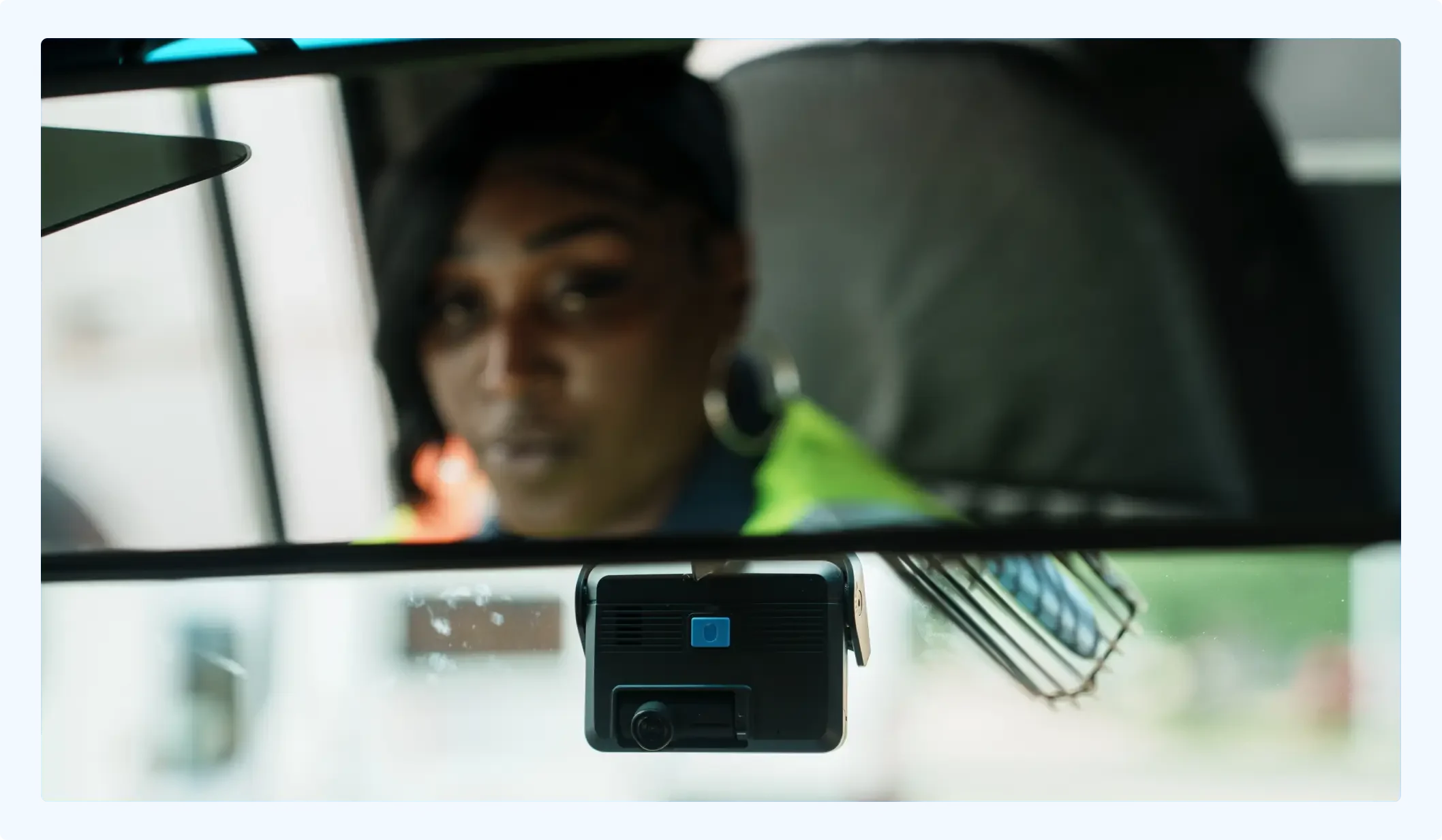 Person in high-visibility clothing visible in rearview mirror with dashboard camera mounted below.