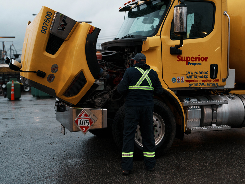 Technicien en gilet réfléchissant inspecte le moteur d'un camion jaune Superior Propane, capot ouvert.
