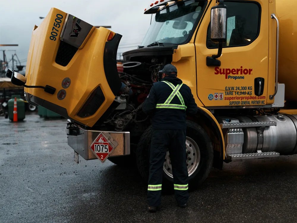 Technicien en gilet réfléchissant inspecte le moteur d'un camion jaune Superior Propane, capot ouvert.