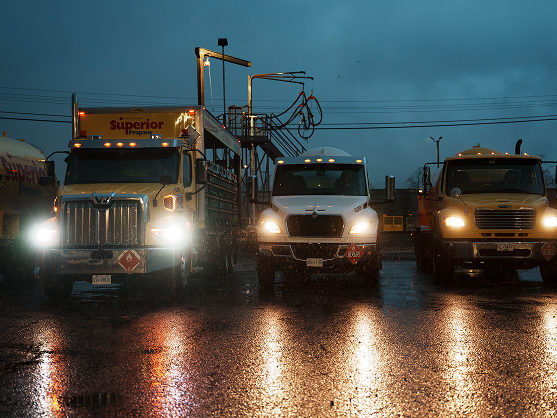 Three Superior Propane trucks with headlights on driving in rainy, dark conditions on a wet road.