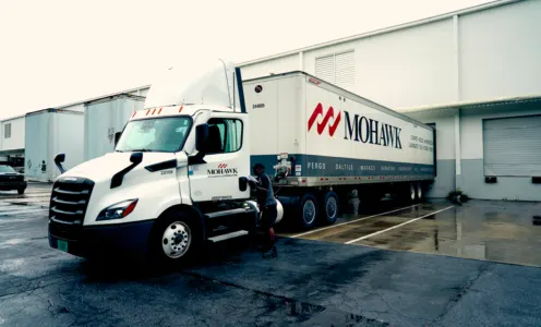 White Mohawk semi-truck with trailer parked at a loading dock on a wet pavement after rain.