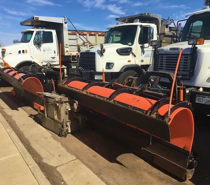 White dump trucks with orange snowplows attached to the front, parked in a row under blue sky.