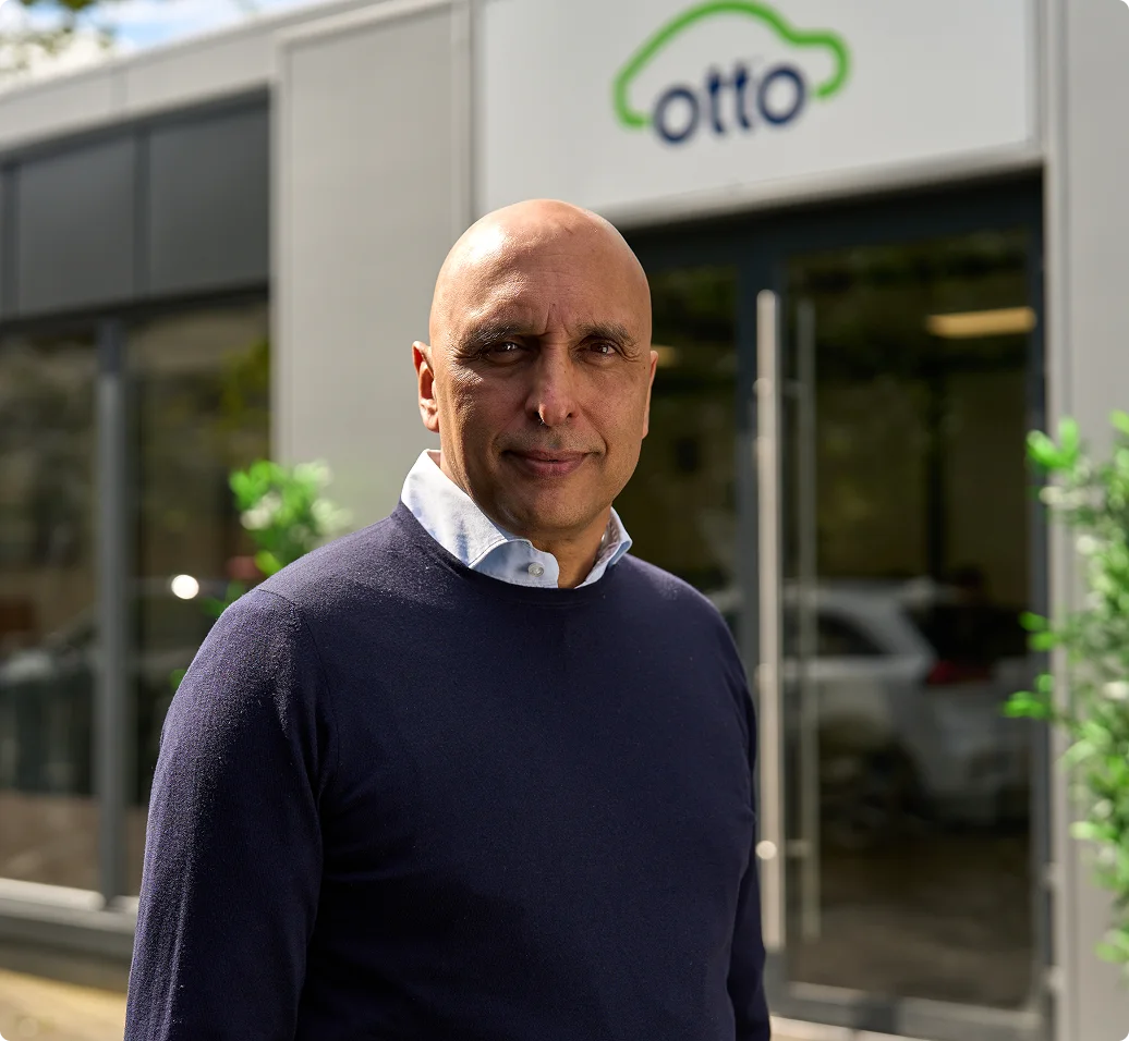 Gurinder Dhillon, CEO und Gründer von Otto Car, steht vor dem Bürogebäude, grüne Wolkenlogo im Hintergrund sichtbar.