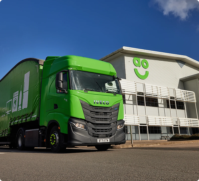 Bright green Iveco delivery truck parked in front of a white building with a green smiley face logo under blue sky.