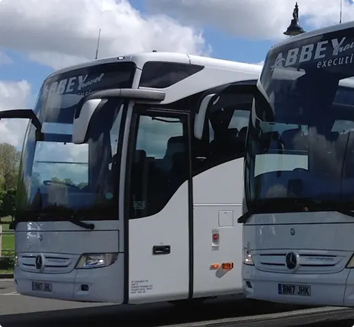 Zwei weiße Abbey Travel Executive Reisebusse stehen nebeneinander unter blauem Himmel.