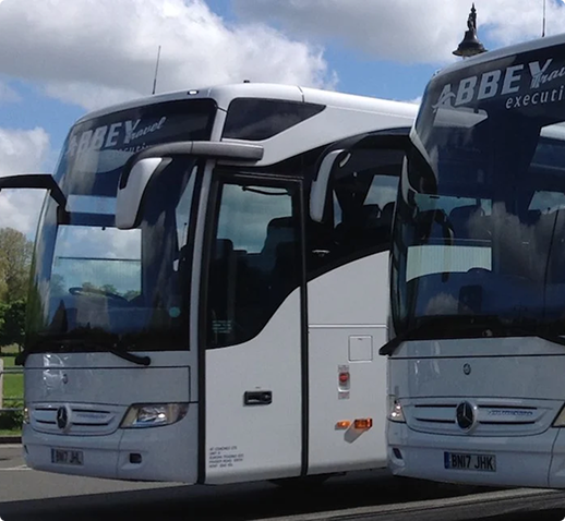 Deux autocars blancs de la compagnie Abbey Travel garés côte à côte sous un ciel nuageux.