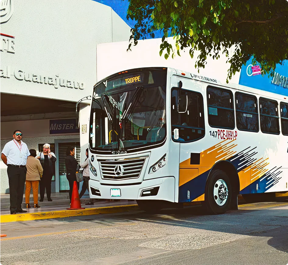 Autobús blanco con detalles amarillos y azules estacionado frente a terminal de Guanajuato con pasajeros esperando abordar.