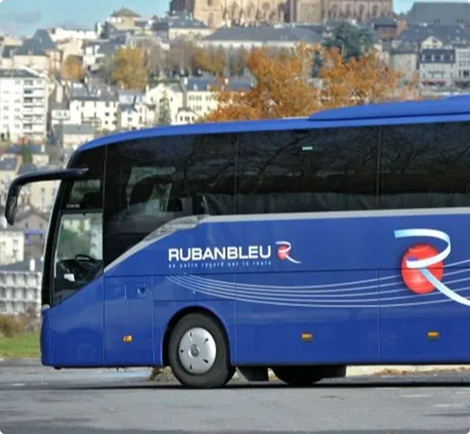 Blue Rubanbleu coach parked with historic European town featuring autumn trees and cathedral in background.