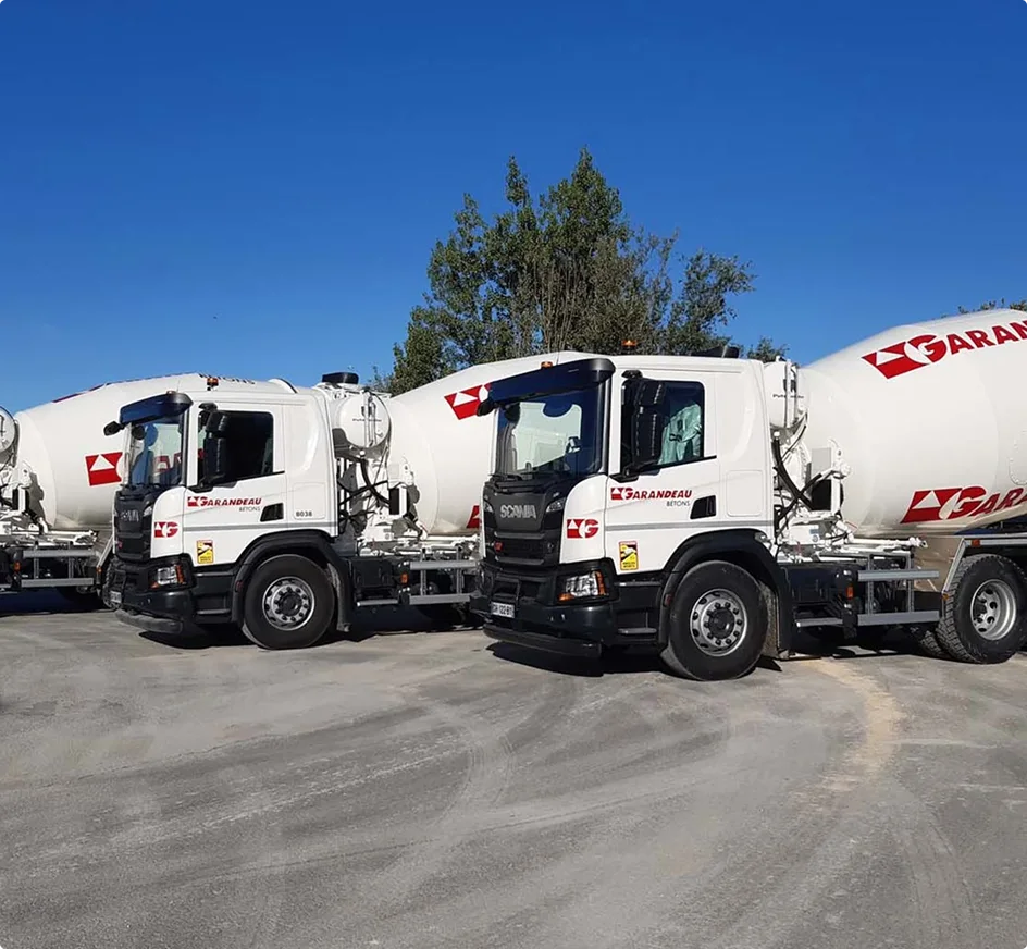 Camions bétonnières blancs de la société Garandeau alignés sur un chantier sous un ciel bleu éclatant.