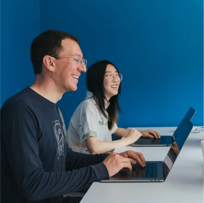Samsara employees sitting at a desk smiling and working at the computer.