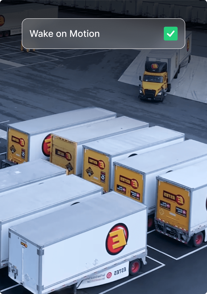 Delivery trucks in parking lot w/mobile app showing 'Wake on Motion' and 'Check-in rate while moving' options enabled.
