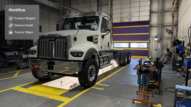 White semi truck in a maintenance facility with workflow steps showing Product Begins, Device Install, and Tractor Ships.