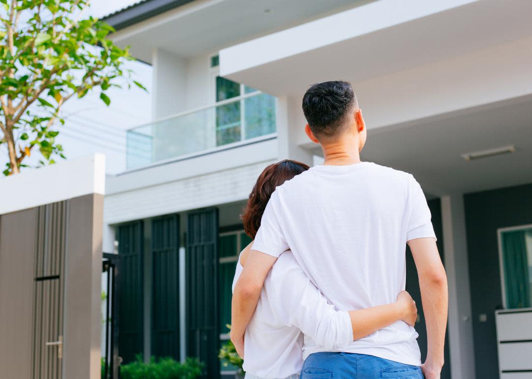 “Photograph of a couple embracing in front of a residential building” - Source: Canva