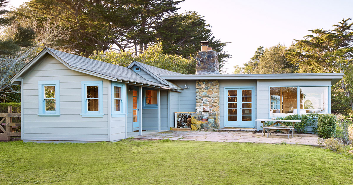 A Light Blue Bungalow Style Home with a Stone Chimney on a Sunny Evening