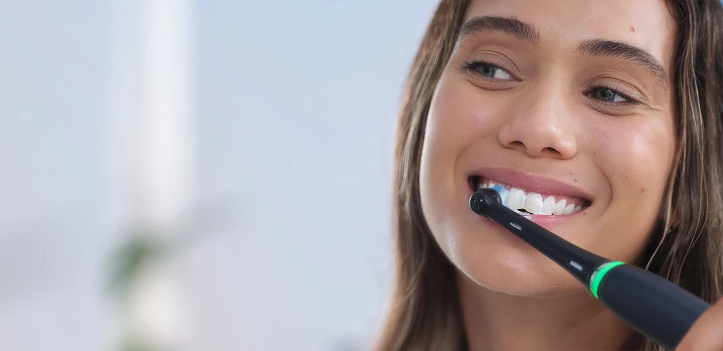 Nainen hymyilee pidellen tavallista Oral-B-hammasharjaa undefined