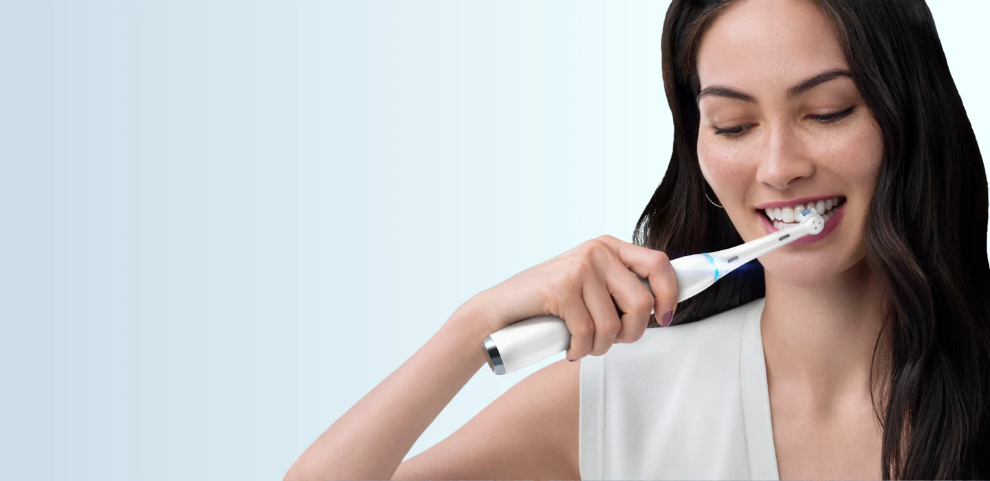 Nainen hymyilee pidellen tavallista Oral-B-hammasharjaa undefined