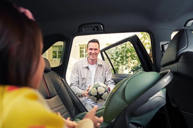 Isä ojentamassa autossa jalkapalloa lapselle
