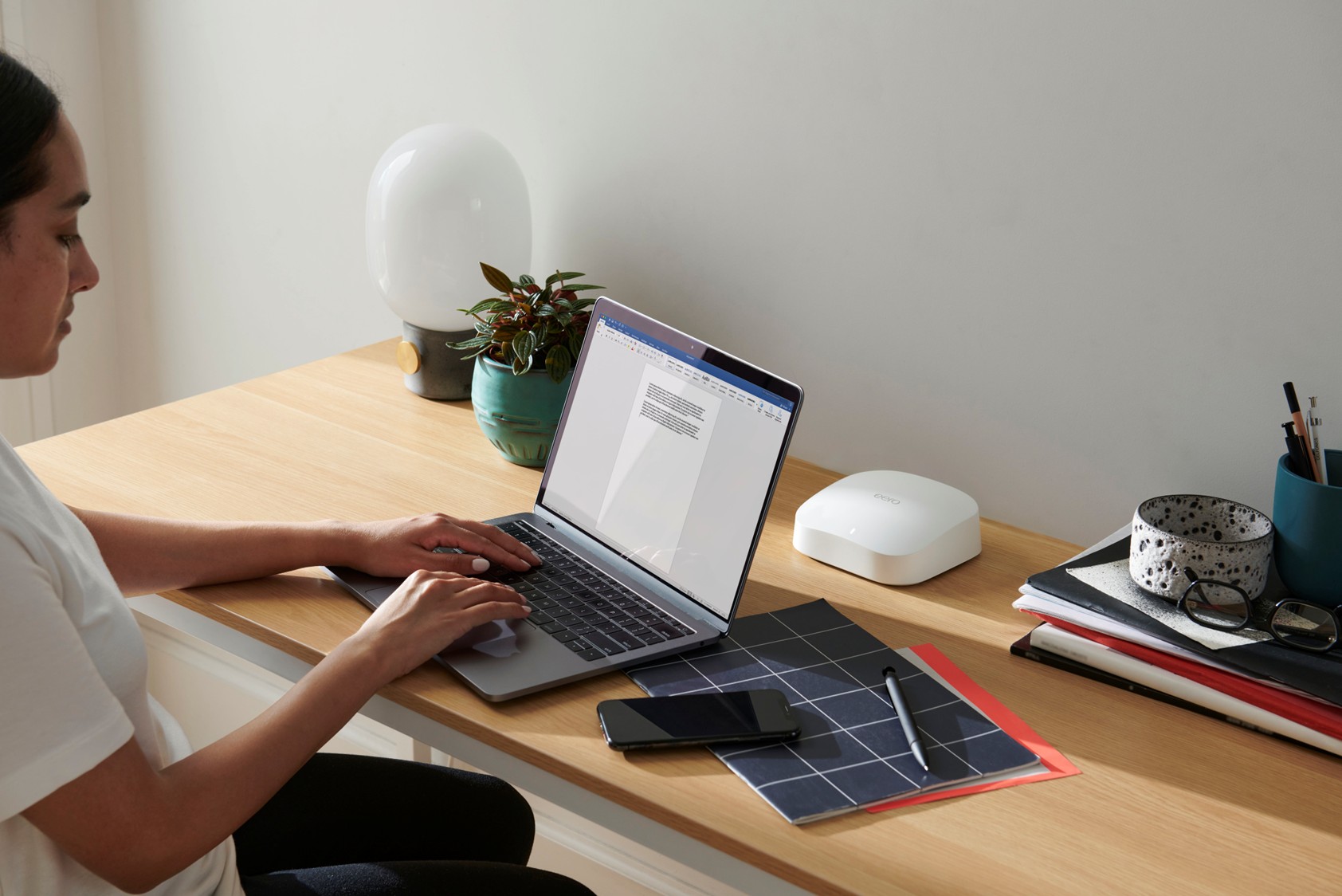 A woman works, sat at her laptop, an eero Pro 6 router is on the desk next to her - LightSpeed Broadband