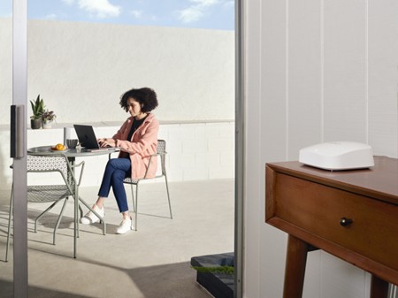A woman sits on her outdoor terrace in the sun, working at her laptop, just inside the house is an eero Pro 6E router - LightSpeed Broadband