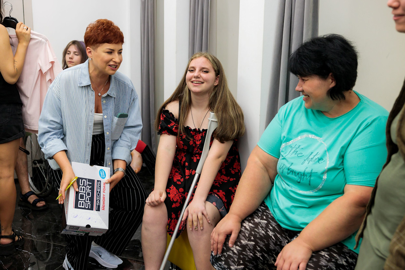 A Ukrainian girl with crutches, she has a war injury, together with SOS carers and parents choosing beautiful clothes. 